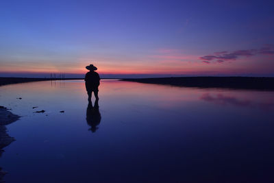 Silhouette man standing in shallow water at beach against sky during sunset
