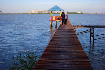 Rear view of people standing on pier over sea