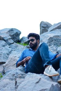 Young man on rock against sky