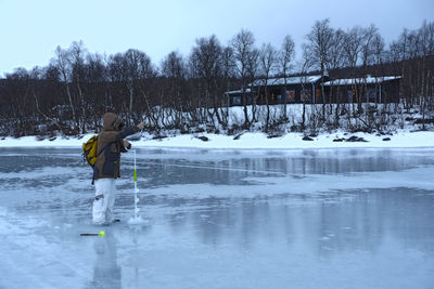 Boy on frozen lake by trees during winter