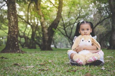 Portrait of innocent girl sitting with stuffed toy at park