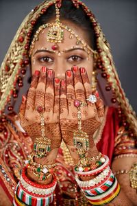 Portrait of bride showing heena tattoo on hands against gray background 