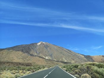 Scenic view of road by mountains against blue sky