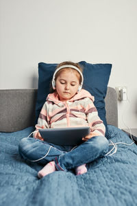 Cute girl using digital tablet sitting on bed at home