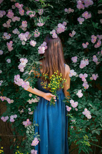 Low section of woman standing by pink flowering plants