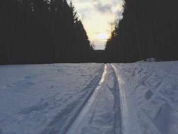 Tire tracks on snow field against sky