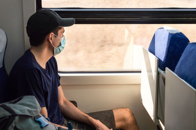 Young man with mask traveling by train during covid-19 pandemic.