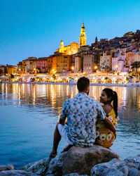 Rear view of people looking at illuminated buildings against sky