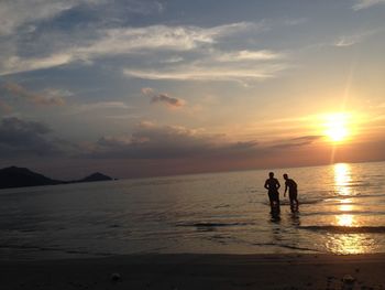 Silhouette people on beach against sky during sunset