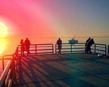 Silhouette people by sea against sky during sunset