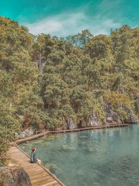 Man sitting on boardwalk at lake against sky