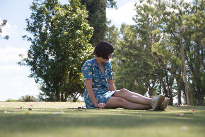 Side view of woman sitting against trees