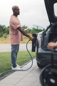 Full length side view of man charging electric car at station