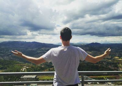 Rear view of young man with arms outstretched standing against sky