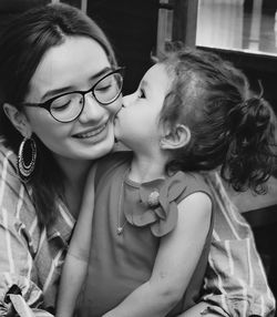 Close-up of cute daughter kissing happy mother at home