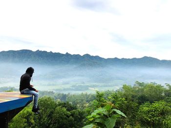 Man sitting on mountain against sky