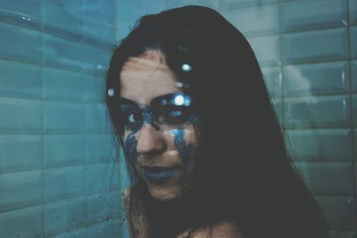 Close-up portrait of young woman with glitters on face against wall