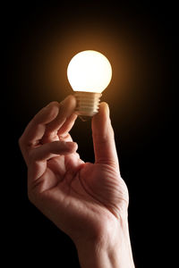 Close-up of hand holding light bulb against black background