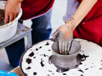 Midsection of people making pot on spinning wheel at workshop