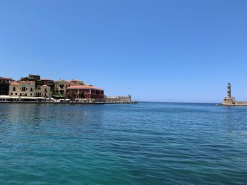 Buildings by sea against clear blue sky