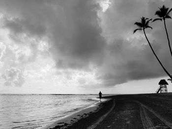 Silhouette man standing on road by sea against sky