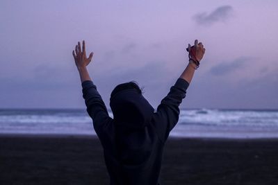 Rear view of person with arms raised standing at parangtritis beach during dusk