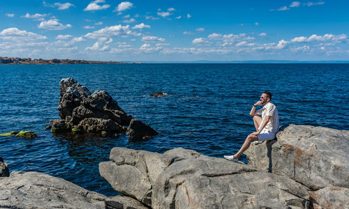 Man standing on rocks by sea against sky