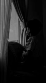 Rear view of woman sitting on bed at home