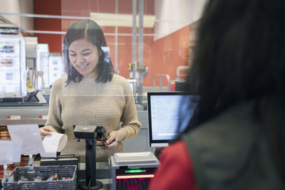 Smiling young female customer taking receipt at checkout in supermarket