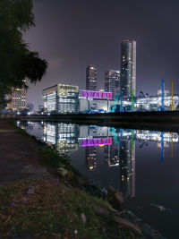 Illuminated modern buildings by river against sky in city at night