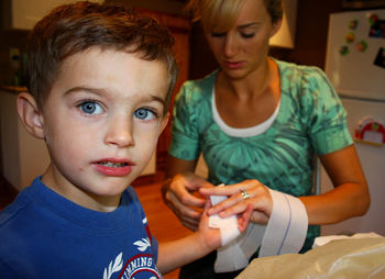 Mother putting bandage on child hand at home