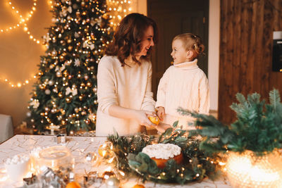 Happy mom and daughter in sweaters together prepare cake for christmas holiday in kitchen at home