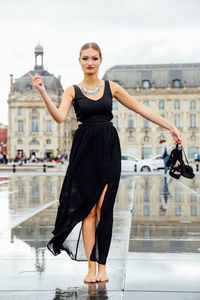 Portrait of confident young woman standing on wet street in city