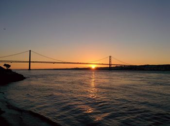 Silhouette april 25th bridge over tagus river against sky during sunset