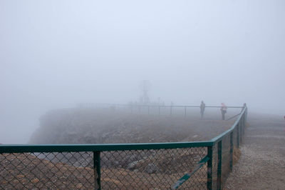 Fence on snow covered land against sky
