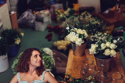 High angle view of woman looking at flowers in container on table at flower shop