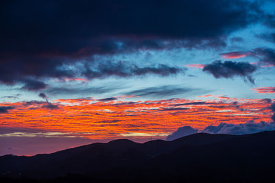 Scenic view of dramatic sky over silhouette mountains during sunset