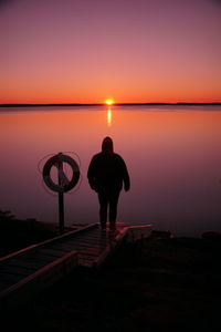 Rear view of silhouette man standing on shore against sky during sunset