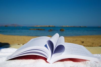 Close-up of open book on beach against blue sky