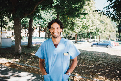 Portrait of smiling male nurse standing with hands in pockets at nursing home