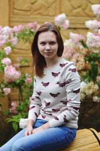 Portrait of woman sitting on bench against plants in yard