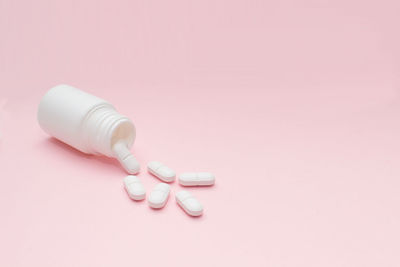 High angle view of pills spilling from bottle against pink background