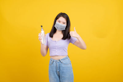 Portrait of beautiful young woman standing against yellow background