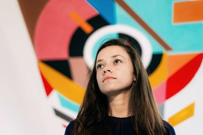 Low angle view of thoughtful beautiful woman standing against multi color wall 