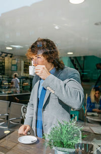 Businessman having drink while standing in cafe at table