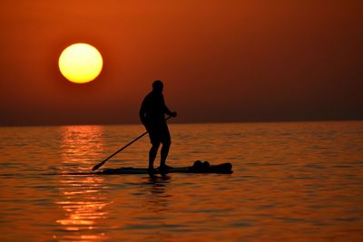 Silhouette people in boat in sea during sunset