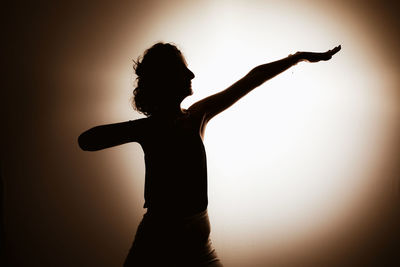 Silhouette woman with arms outstretched standing against sky during sunset