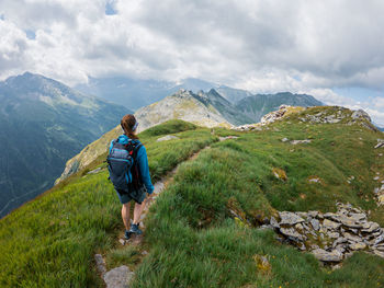 Rear view of woman hiking on rocky mountain peak against sky