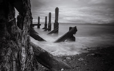 Abandoned wooden structure at beach against cloudy sky