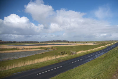 Scenic view of road passing through countryside landscape against cloudy sky